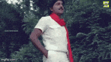 a man wearing a red scarf and a white shirt is standing in the woods .