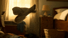 a person is jumping in the air in a bedroom with a lamp on the nightstand