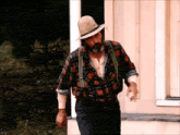 a man in a plaid shirt suspenders and a hat