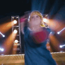 a woman in a blue dress is dancing on a stage with lights behind her