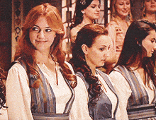 a group of women standing next to each other with one wearing a white shirt and a blue vest