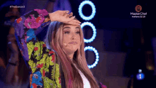 a woman in a colorful jacket stands in front of a microphone and a masterchef logo