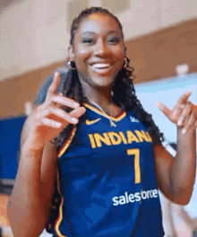 a woman wearing a blue and yellow basketball jersey is smiling and giving a peace sign .