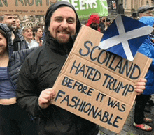 a man holds up a sign that says scotland hated trump before it was fashionable
