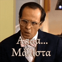 a man wearing glasses and a suit has the words " aaa ... maliota " written on the bottom