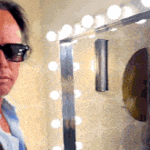 a man wearing sunglasses stands in front of a wall with lights on it