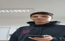 a young man wearing a black hoodie holds a cell phone
