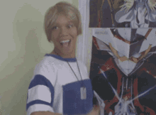a man with blonde hair is standing in front of a wall with a picture of a robot behind him