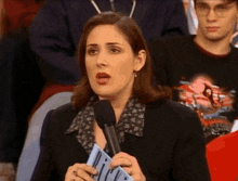 a woman speaking into a microphone while holding a piece of paper that says r.i.p.