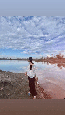 a woman stands on the shore of a lake with a blue sky in the background