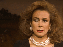 a woman wearing a pearl necklace and earrings looks serious
