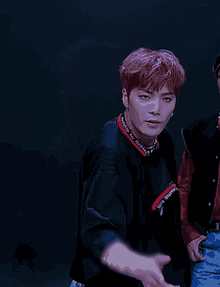 a young man with purple hair is wearing a black shirt with a red trim