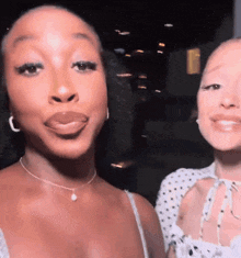 two women are standing next to each other and one has her tongue out .