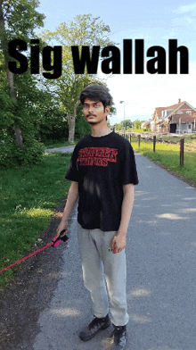 a man wearing a black shirt that says stranger things is walking a dog on a leash