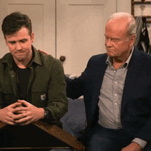 two men are sitting next to each other on a couch . one of the men is wearing a suit .