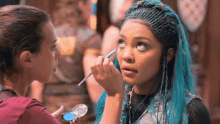 a girl with blue hair is getting her makeup done by a makeup artist .