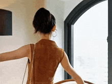 a woman in a brown dress is standing in front of a window with the word njz on the back
