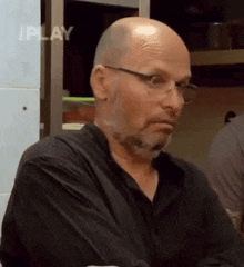 a bald man with glasses and a beard is looking at something .