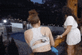 two women are standing next to each other on a deck with a swimming pool in the background .