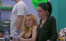 two women are sitting next to each other in a room with a man standing behind them .