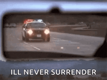 a police car is driving down a highway in a rear view mirror with the words `` ill never surrender '' below it .