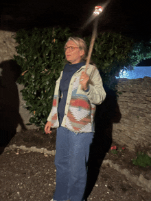 a woman wearing a native american jacket holds a stick