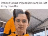 a young man in an orange hoodie is talking about himself in his room