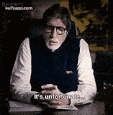 a man with glasses and a beard is sitting at a desk and talking .