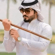 a man with a beard and sunglasses is holding a stick in his hand .