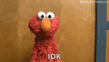 elmo from sesame street says idk in front of a wooden wall .