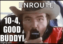 a man in a cowboy hat is talking on a cell phone and says `` enroute 10-4 , good buddy ! ''