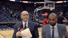a man in a suit and tie is holding a piece of paper in front of a basketball court .