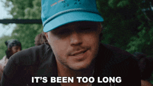a man wearing a blue hat with the words it 's been too long below him
