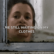a woman is looking out a window with the words " me still waiting on my clothes " below her