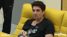 a man sitting on a yellow couch with a shocklat logo on the bottom right