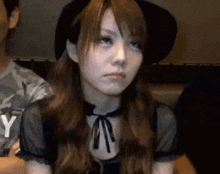 a woman wearing a black hat and a black dress is making a sad face .
