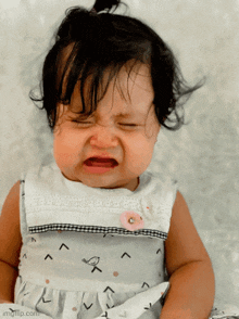 a baby girl is crying with her eyes closed and a pink flower on her neck
