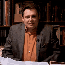 a man sitting in front of a bookshelf that has a book titled art of war on it