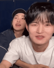 two young men are sitting next to each other and one has a hat on