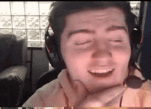a man wearing headphones and a microphone is smiling with his eyes closed and his hand on his chin .