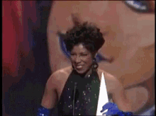 a woman in a black dress and blue gloves is smiling while speaking into a microphone