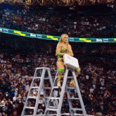 a woman stands on a ladder in front of a crowd that is watching a wrestling match sponsored by amazon prime