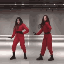 two women in red jumpsuits are dancing in a dance studio .