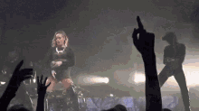 a woman is dancing on a stage in front of a crowd while a man stands behind her .