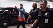 a man in a denim jacket is walking with two police officers in front of a black suv