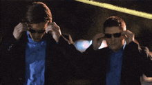 a man in a suit and sunglasses adjusts his sunglasses