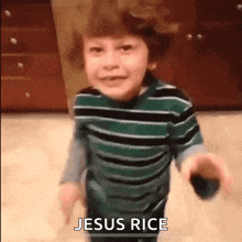 a young boy in a green and black striped shirt is holding a black object and saying jesus rice .