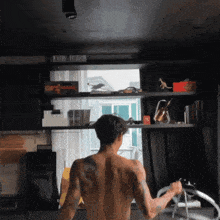 a man with a tattoo on his back is standing in front of a bookcase