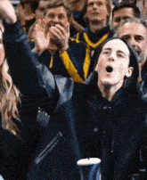 a woman in a black jacket is sitting in a crowd of people with her mouth open