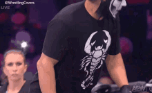 a man wearing a black shirt with a scorpion on it is walking in a wrestling ring